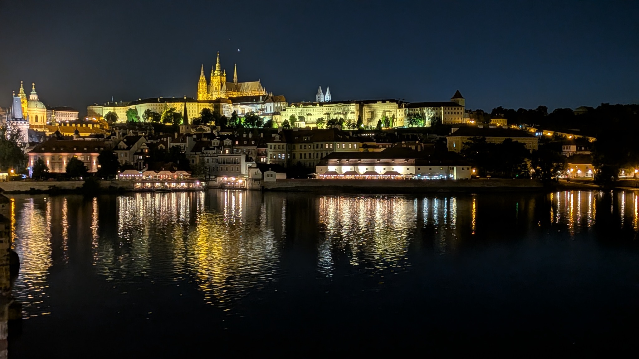 Prague Castle lit up at night with reflections on the Vltava river